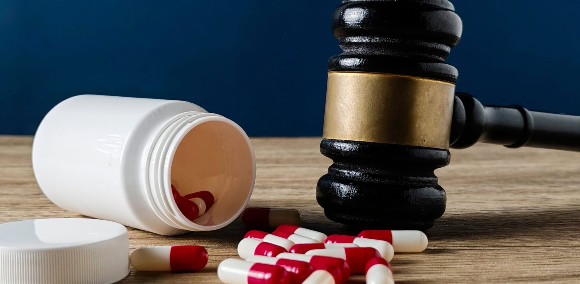 Gavel and Spilled Red and White Capsules from a Medicine Bottle Symbolizing Drug Law and Regulation. By MohamadFaizal - AdobeStock