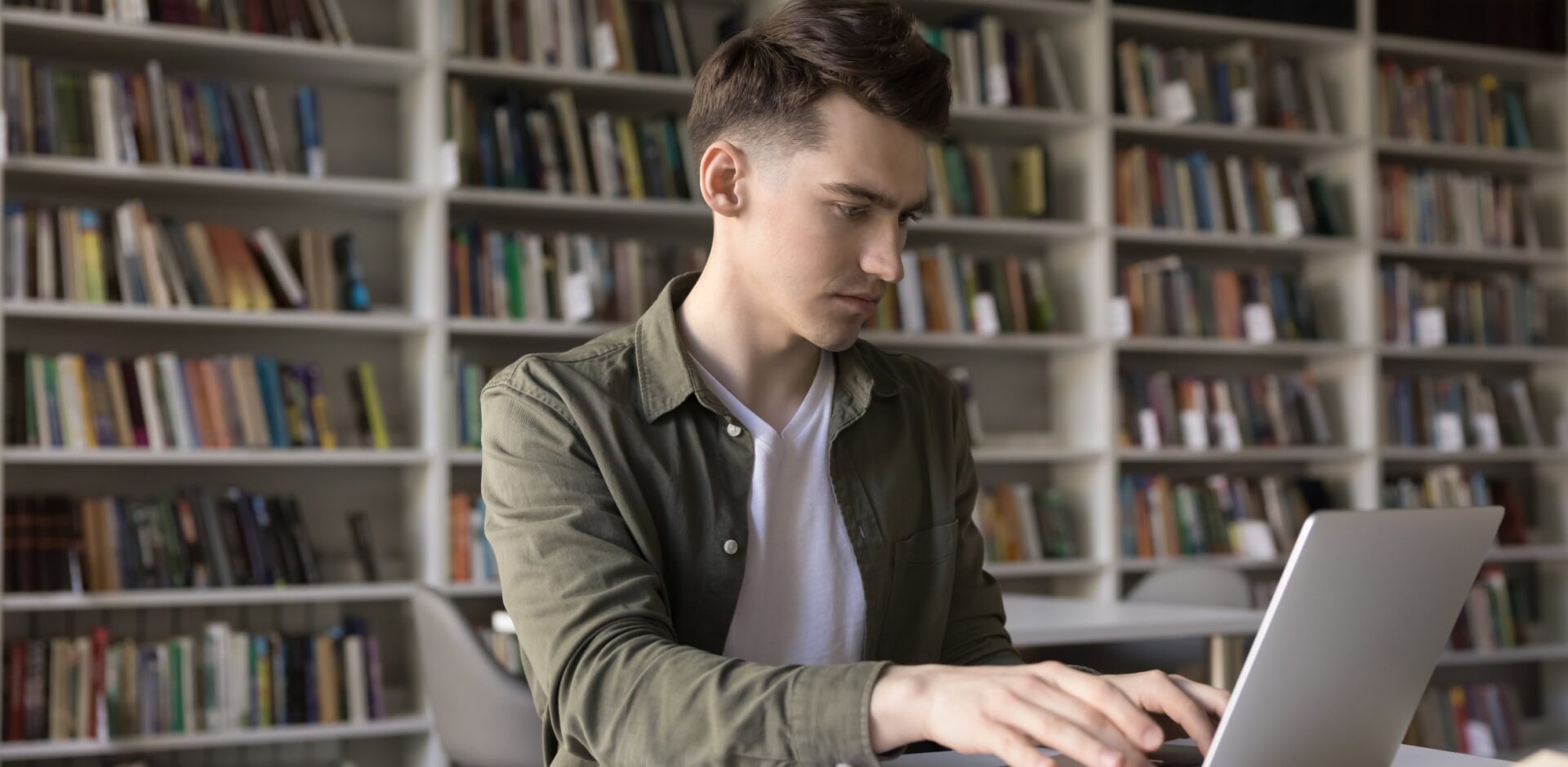 Remote learning. Busy young college student work at library table write essay coursework project assignment on notebook pc using information from paper scientific literature personal handwritten notes. By fizkes - AdobeStock